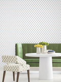 Sure! Here’s a rewritten version of the sentence using your product data: A green tufted sofa, a round white table adorned with flowers and books, and a patterned chair are arranged against a white wall covered in Serene Villa Floral Stamp Wallpaper by York Wallcoverings.