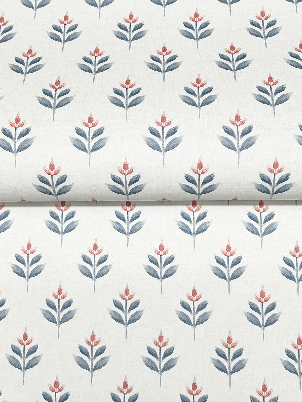 The Serene Villa Floral Stamp Wallpaper by York Wallcoverings features a repeating pattern of stylized flowers with red petals and blue leaves set against a white background, with the design printed on wallpaper that shows a visible horizontal fold near the middle.