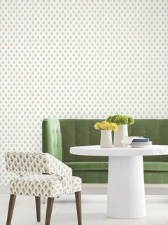 A green velvet sofa, a round white table adorned with yellow flowers in vases, and a patterned chair are arranged against a wall covered in York Wallcoverings’ Serene Villa Floral Stamp Wallpaper, featuring a delicate, small-scale floral motif. The floor is tiled in white.
