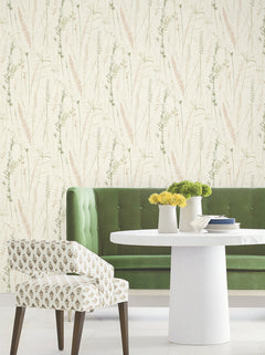 A green tufted sofa, white round table with yellow flowers, and patterned chair sit against Meadow Splendor Botanical Wallpaper with a delicate grass motif in soft beige and green tones.