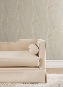 A beige upholstered sofa with a round pillow sits on a cream rug in front of Meadow Splendor Botanical Wallpaper featuring a subtle, light botanical pattern.