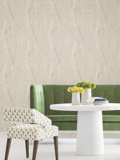 A green tufted sofa, white round table, and patterned chair sit in front of Meadow Splendor Botanical Wallpaper. Yellow flowers in small vases decorate the table.