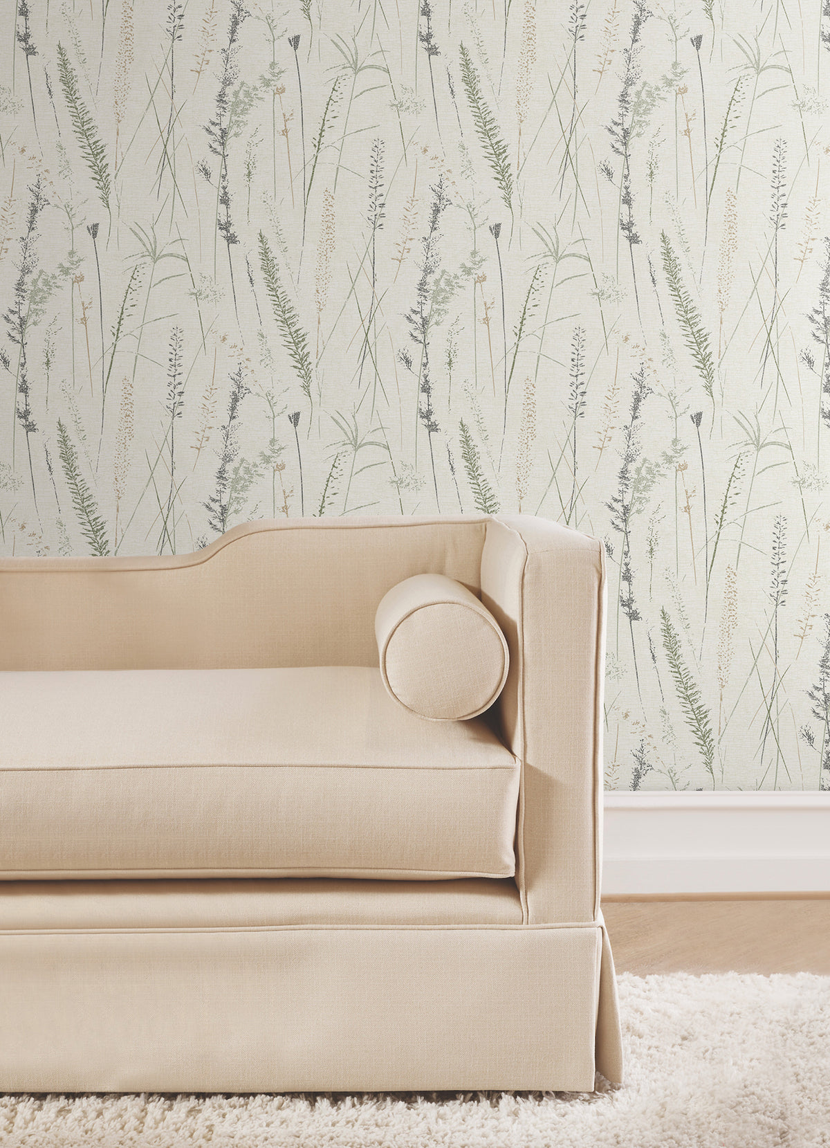 A beige sofa with a cylindrical cushion sits in front of Meadow Splendor Botanical Wallpaper, which features a delicate pattern of grasses and plants in light tones.