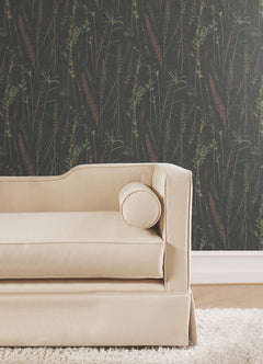 Beige upholstered sofa with a round cushion in front of Meadow Splendor Botanical Wallpaper, featuring subtle botanical patterns, placed on a light-colored floor next to a white baseboard.
