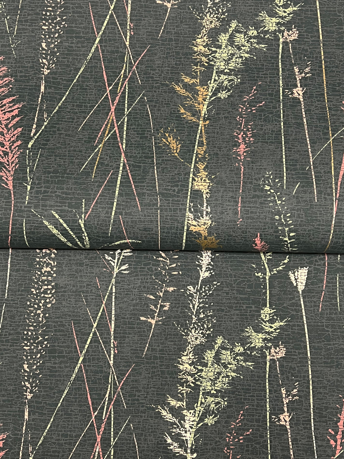 Meadow Splendor Botanical Wallpaper features a dark background adorned with delicate, pastel-colored grasses and wildflowers arranged in vertical patterns. A visible seam is present, running horizontally across the center of the image.