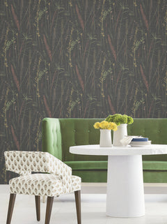 A modern dining area with a green velvet tufted bench, a white round table topped with yellow flowers, a patterned chair, and dark Meadow Splendor Botanical Wallpaper.