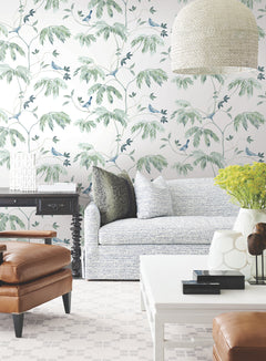 Living room featuring the Cillian Botanical Bird Trail Wallpaper by York Wallcoverings, a patterned sofa, leather chair, black side table, white coffee table, modern decor accents, a large pendant light, and a vase of yellow flowers on the table.