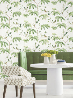 Green velvet bench and patterned chair surround a white round table with yellow flowers, set against York Wallcoverings’ Cillian Botanical Bird Trail Wallpaper.