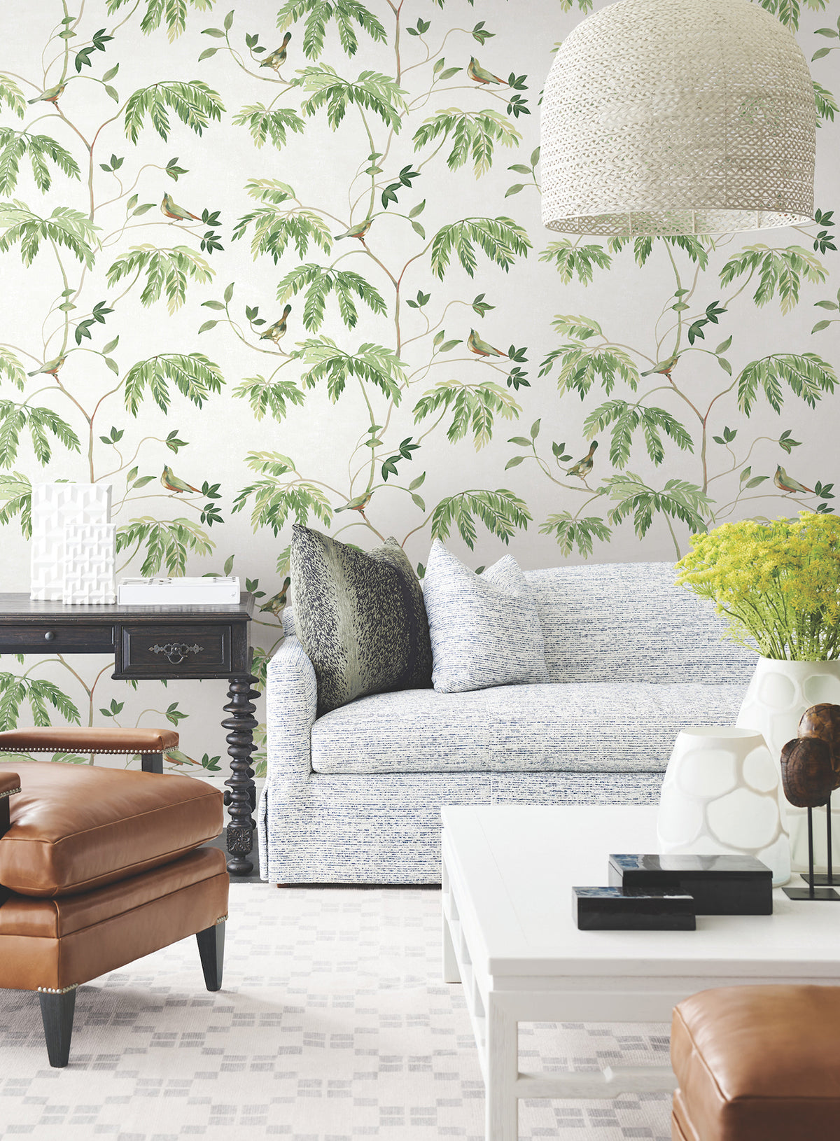 Bright living room featuring a light blue sofa, brown leather chairs, and a white coffee table against Cillian Botanical Bird Trail Wallpaper by York Wallcoverings. Decorative pillows, green-yellow flowers, and a modern white lamp complete the stylish and inviting space.