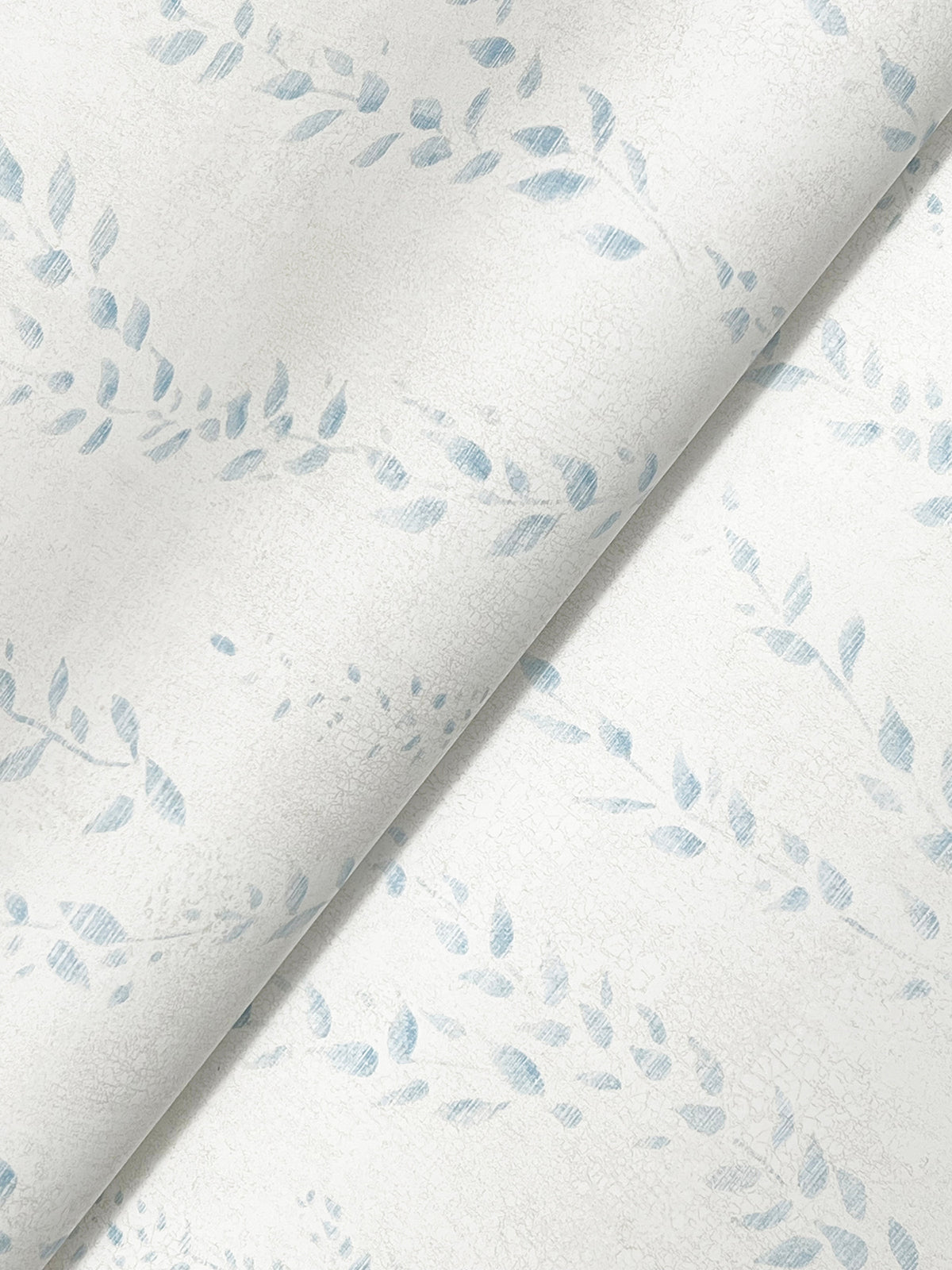 A close-up of the Alpenrose Vine Wallpaper by York Wallcoverings, featuring light-colored paper with a gentle cracked texture and a soft blue leafy vine design, shown at an angle with a visible crease or fold.