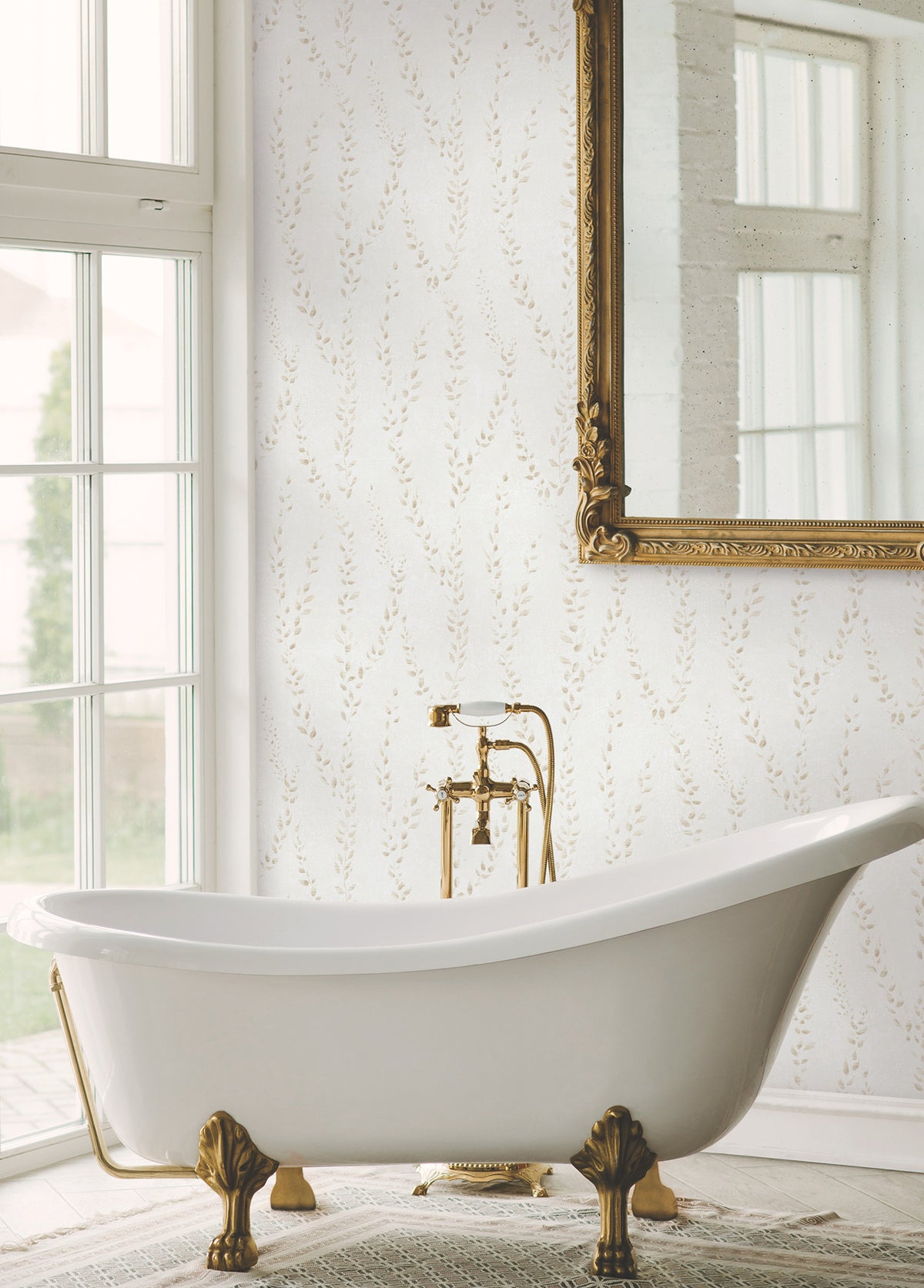 Elegant bathroom with a white clawfoot tub, gold fixtures, a large ornate mirror, Alpenrose Vine Wallpaper by York Wallcoverings, and a window letting in natural light.