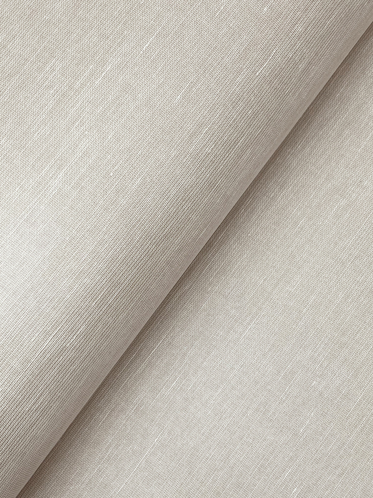 A close-up of York Wallcoverings’ Hempfield Weave Loomed Wallpaper in a light beige shade showcases its subtle, textured pattern. The wallpaper is displayed with a diagonal fold, highlighting the fine horizontal and vertical threads that create its woven look. The surface appears smooth with a gentle sheen.