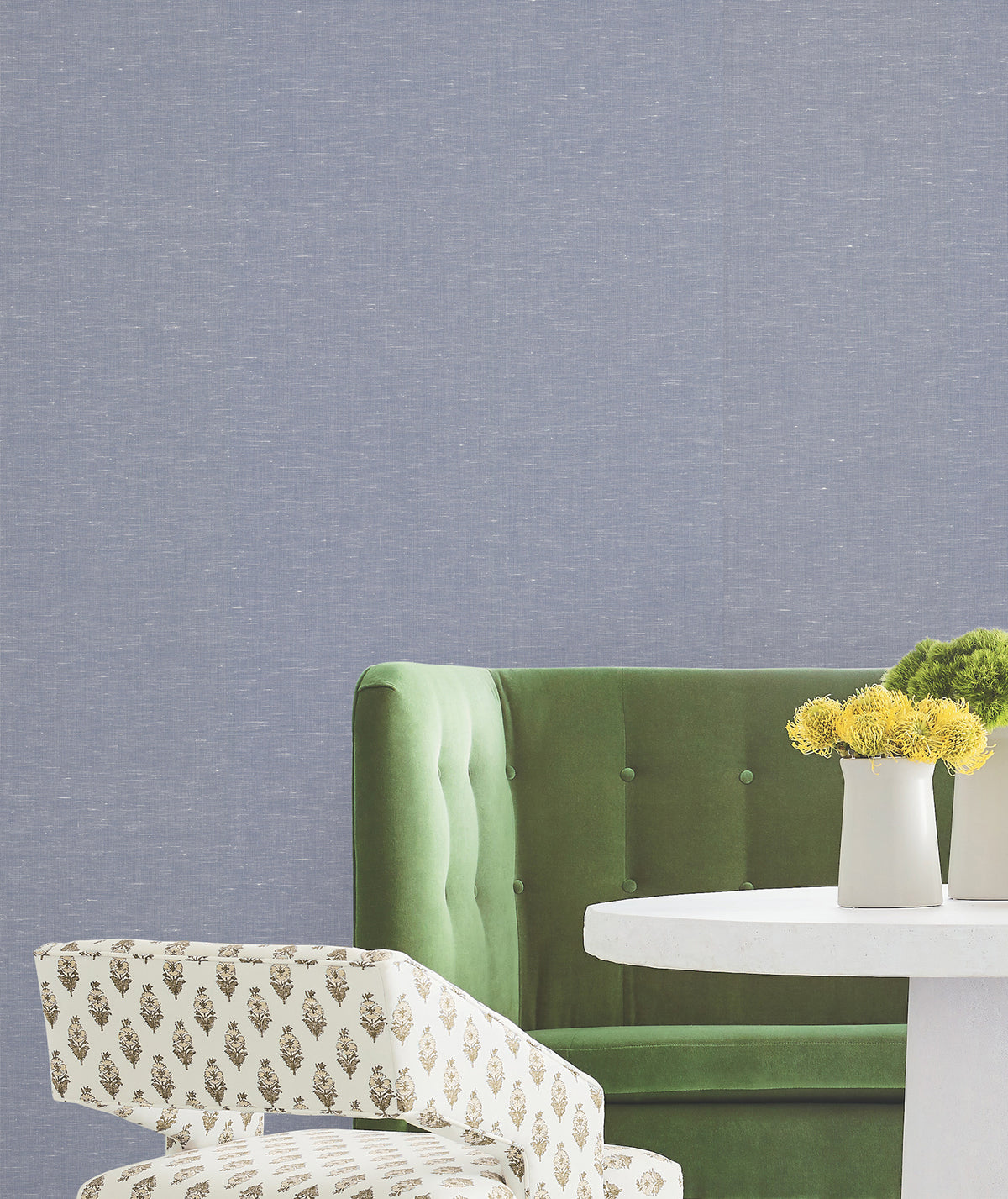 A green sofa, a patterned chair, a round white table, and a vase with yellow flowers are set against a light blue York Wallcoverings Hempfield Weave Loomed Wallpaper.