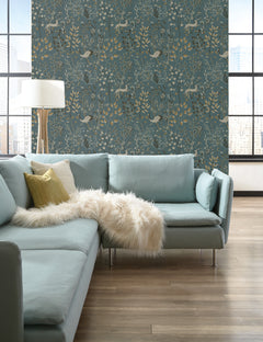A light blue sectional sofa sits in a room featuring Aspen Wallpaper by York Wallcoverings, which displays a pattern of birds and foliage against a dark teal background.