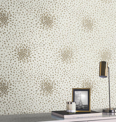 A modern desk is styled with a gold lamp, a framed black-and-white photo of the Eiffel Tower, and stacked books. Behind, York Wallcoverings’ Petite Leaves Wallpaper adds elegance with its gold floral pattern on a light background.