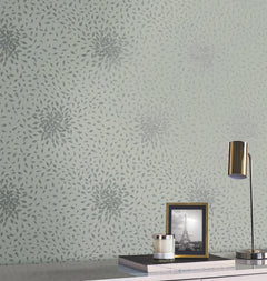 A wall decorated with York Wallcoverings’ Petite Leaves Wallpaper in a gray floral burst pattern on pale green sets the backdrop for a white desk, which displays a gold lamp, a glass candle, and a framed black and white photo of the Eiffel Tower.