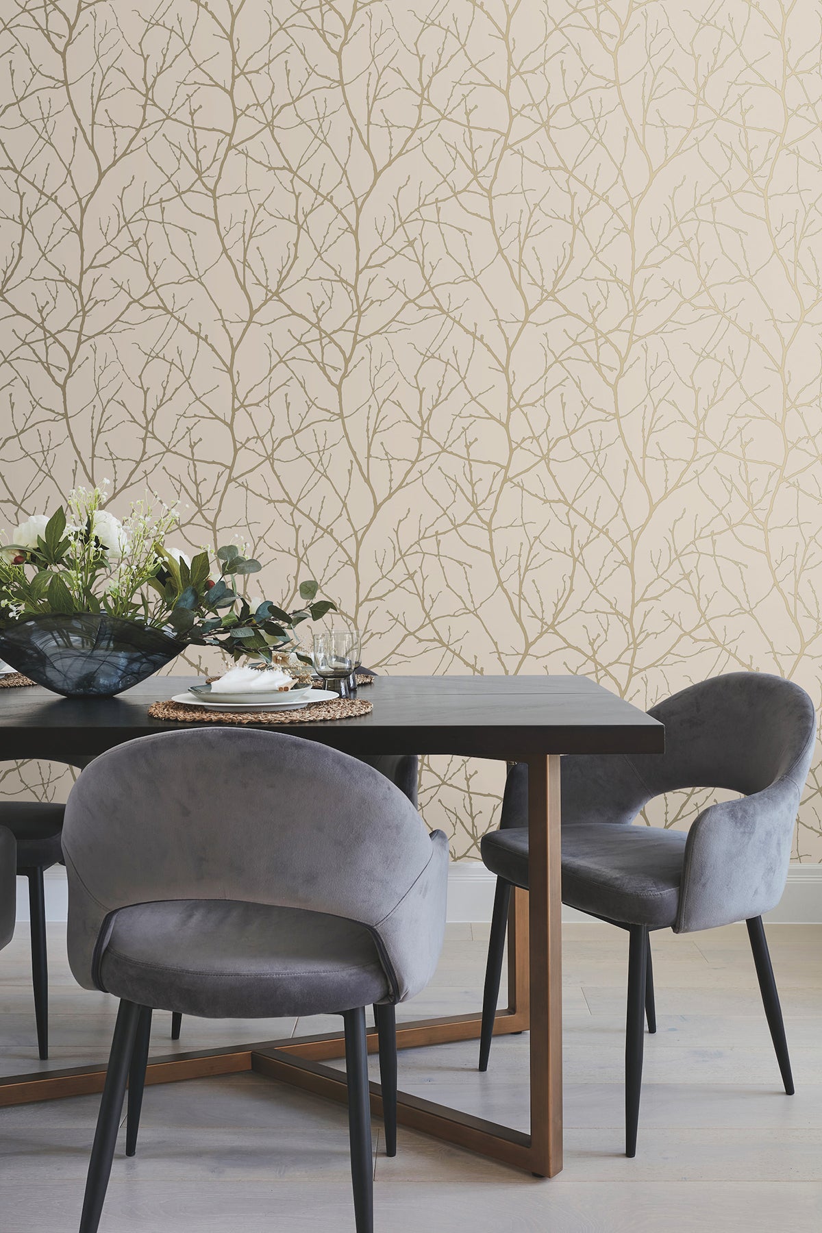 Modern dining area with a dark table, grey velvet chairs, a glass bowl with flowers, and beige Trees Silhouette Wallpaper by York Wallcoverings featuring a delicate tree branch pattern.