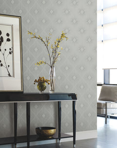 A modern, minimal living room features a black console table with a glass vase holding yellow flowers, a bowl of fruit, and a framed nature print on the wall above Harlowe Wallpaper by York Wallcoverings.