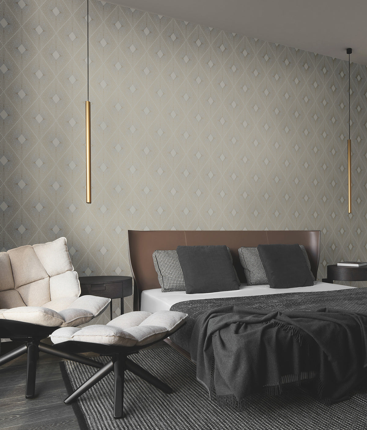 A modern bedroom featuring Harlowe Wallpaper by York Wallcoverings, a brown and white bed with gray pillows, a cream sofa, two footstools, and two slim gold pendant lights hanging from the ceiling.
