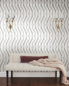 Sure! Here’s your revised sentence incorporating the product data: A tufted cream bench with a mauve pillow and folded throw blanket sits in front of the Graceful Geo Wallpaper by York Wallcoverings. Two brass wall sconces with white lampshades are mounted above the bench, while a dark wooden floor grounds the space.