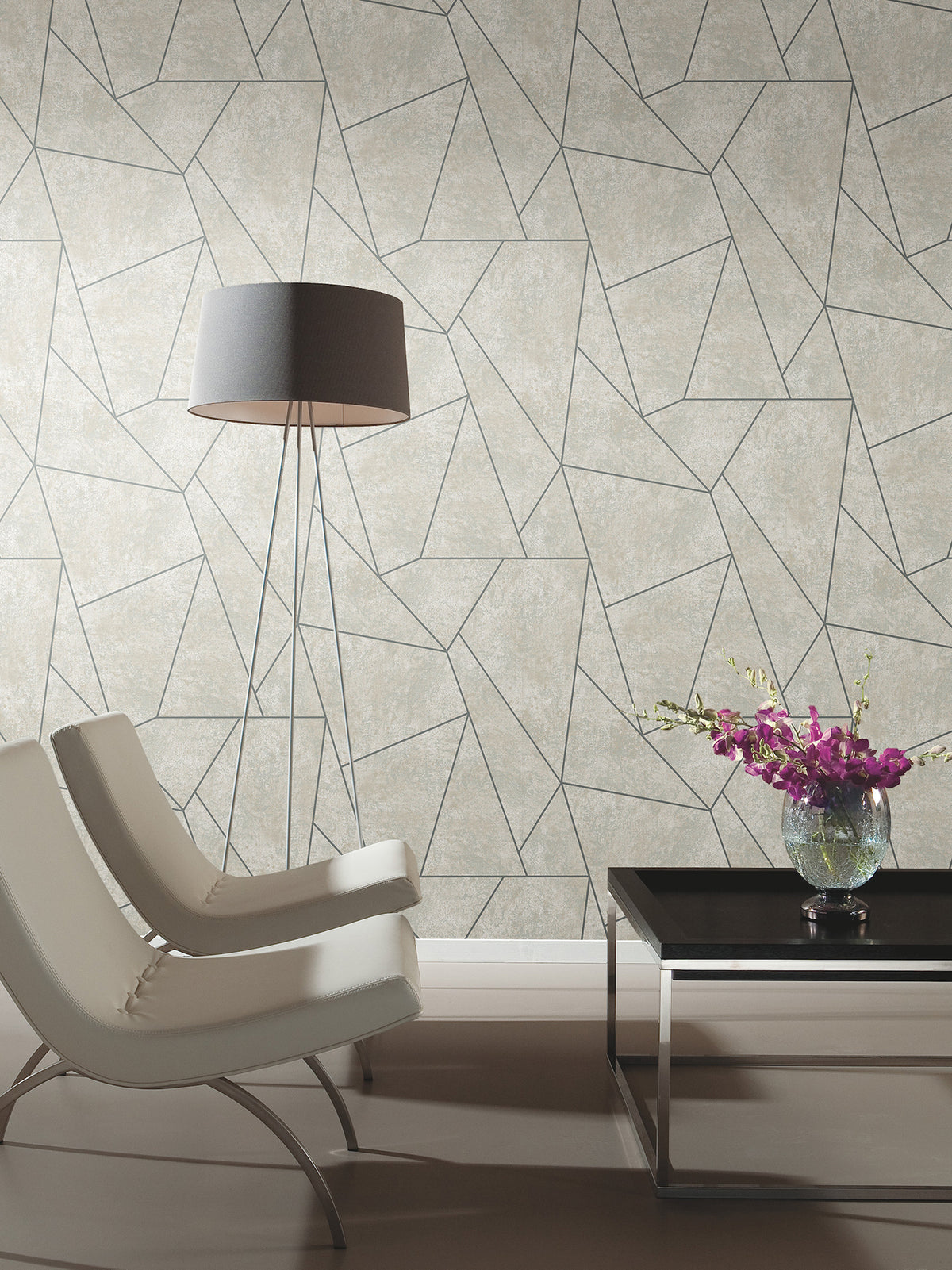 Two modern white chairs, a tall floor lamp, and a black coffee table with a vase of purple flowers sit in front of Nazca Wallpaper by York Wallcoverings in a minimalist room.