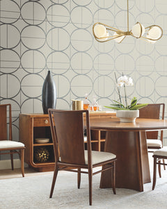 Modern dining room with a wooden table and chairs, a sideboard adorned with decor items, Sun Circles Wallpaper by York Wallcoverings featuring a geometric pattern, an orchid centerpiece, and a gold chandelier with round glass shades.