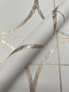 A close-up of the Sun Circles Wallpaper by York Wallcoverings in white, featuring metallic gold geometric lines and an abstract curve pattern, with a rolled-up section visible.