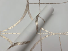 A roll of York Wallcoverings Sun Circles Wallpaper, featuring a white background with a metallic gold geometric pattern of intersecting curved and straight lines, lies partially unrolled atop matching wallpaper.