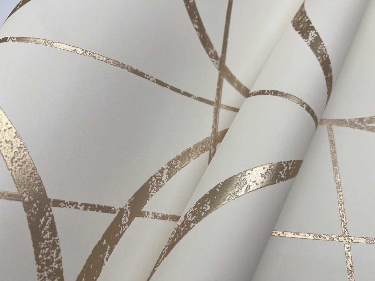 Close-up of York Wallcoverings’ Sun Circles Wallpaper, featuring textured white paper with metallic gold curved and straight lines forming an abstract geometric pattern. The wallpaper appears to be slightly folded or layered.