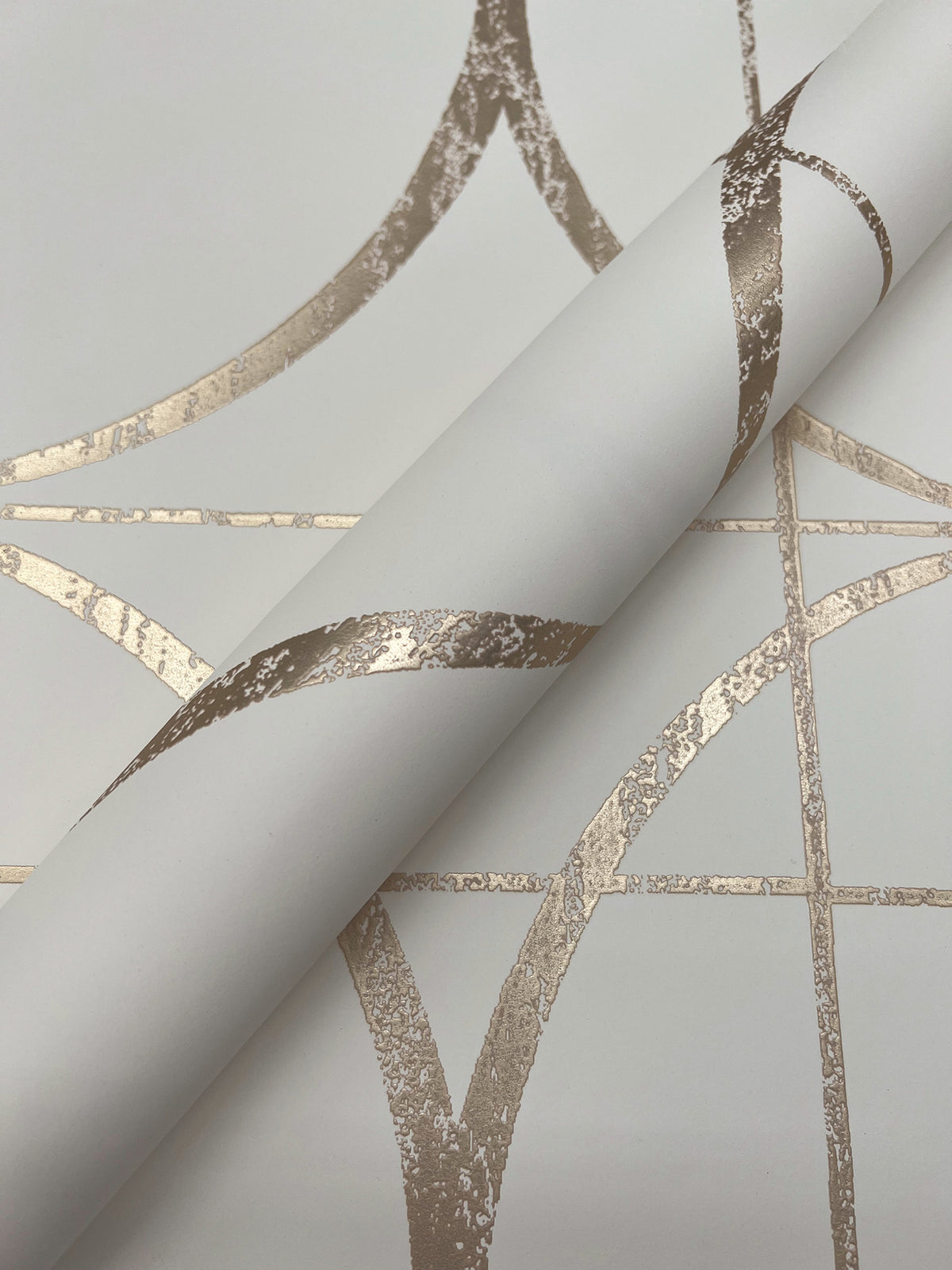 A close-up of the Sun Circles Wallpaper by York Wallcoverings, showcasing its metallic gold geometric pattern with intersecting lines and curved shapes on a crisp white background.