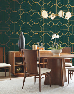 A modern dining room featuring York Wallcoverings’ Sun Circles Wallpaper in dark green and gold geometric patterns, paired with a wooden table and chairs, a sideboard adorned with decor items, and a white orchid centerpiece beneath a contemporary light fixture.