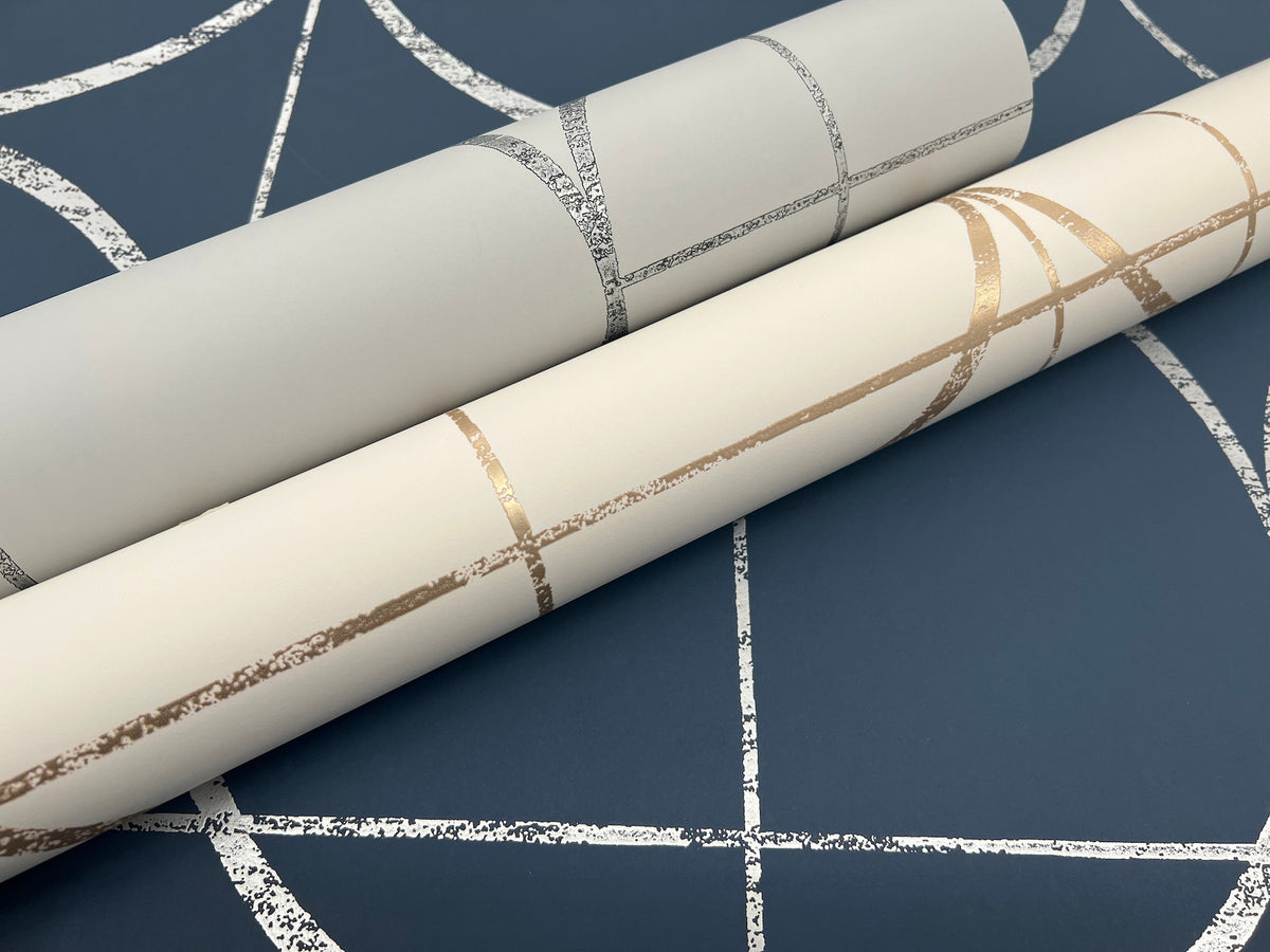 Two rolls of Sun Circles Wallpaper by York Wallcoverings, featuring metallic and textured line designs—one in silver on light gray and the other in gold on cream—are displayed on a blue background with a coordinating white abstract line pattern.
