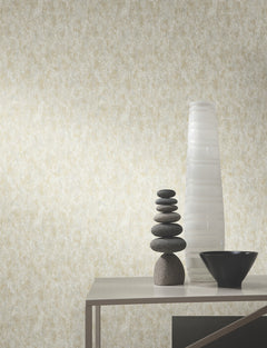 A modern table displays stacked smooth stones, a tall white textured vase, and a black geometric bowl, set against Shimmering Patina Wallpaper by York Wallcoverings.