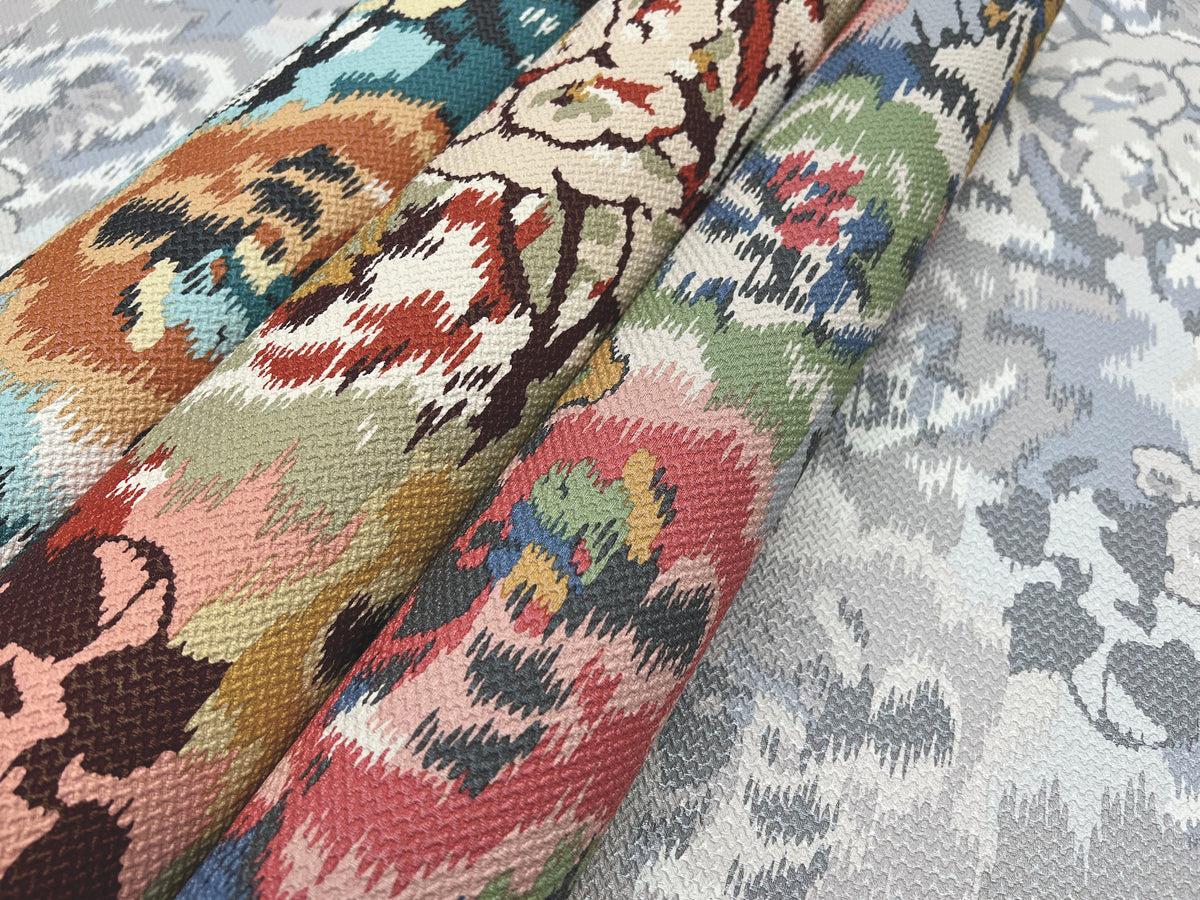 Three rolls of York Wallcoverings’ Flower Pot Wallpaper, each showcasing vibrant floral motifs in shades of red, green, blue, pink, and beige, are arranged side by side on a surface with a subtle, pale floral design.