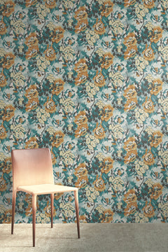A light wooden chair stands on a beige carpet in front of a wall covered in York Wallcoverings’ Flower Pot Wallpaper, featuring colorful, abstract floral patterns in shades of blue, yellow, gray, and white.