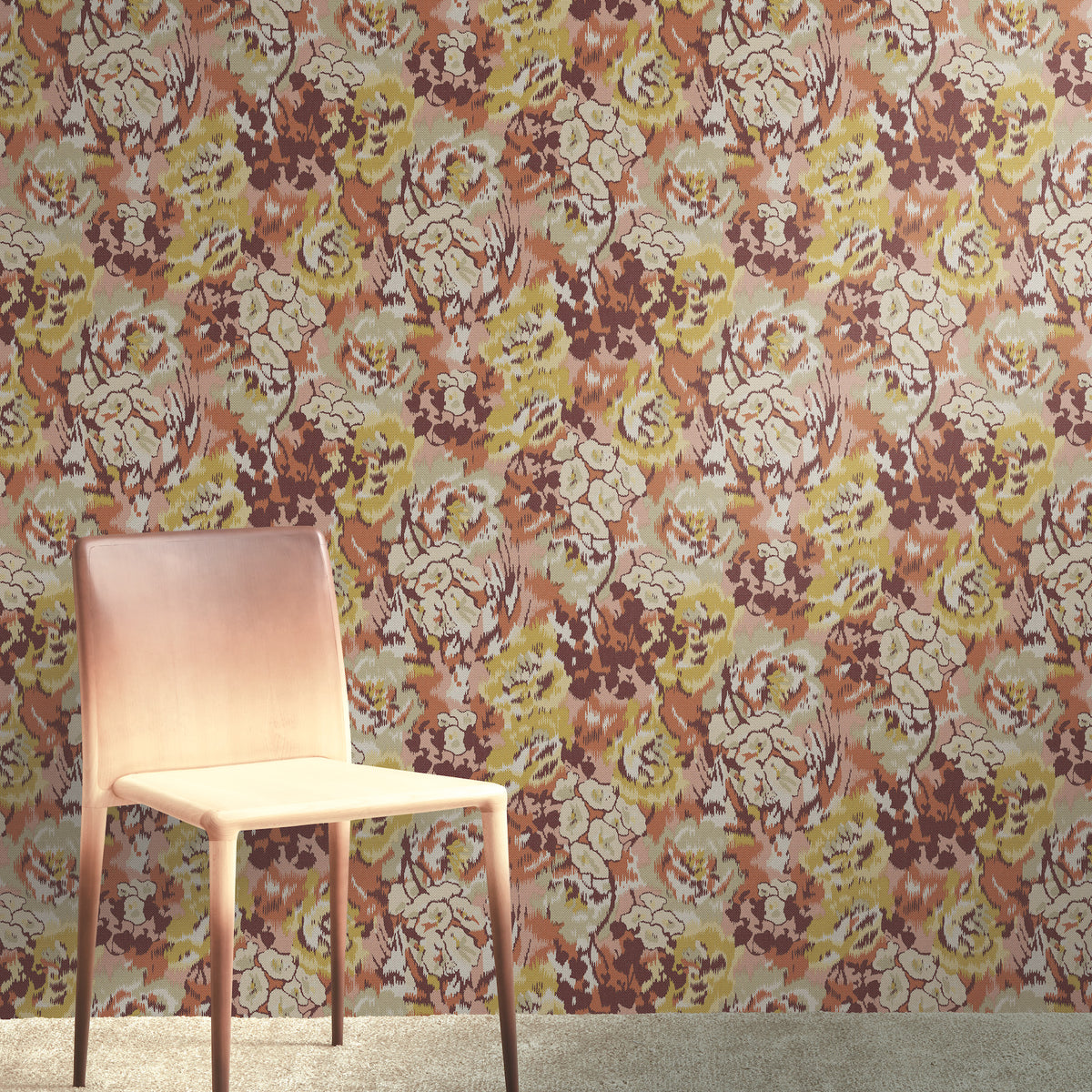 A light pink chair sits on a beige carpet in front of York Wallcoverings’ Flower Pot Wallpaper, which features a floral pattern in shades of pink, brown, and yellow.