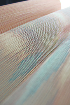 Close-up of Sunrise Flame Wallpaper by York Wallcoverings, featuring a textured surface with fine horizontal lines and a mix of peach, blue, and green hues that create an abstract, wavy design.