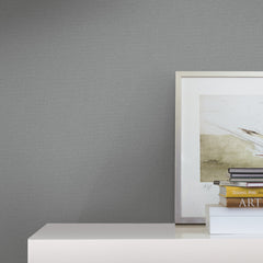 Framed artwork and stacked books sit on a white surface against a wall adorned with Chevronette Wallpaper by York Wallcoverings, creating a minimalist and modern decor scene.