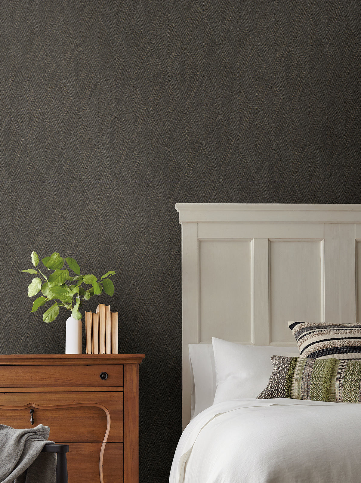 Magnolia Home Challenger Wallpaper features a fine, repeating dark gray chevron pattern behind a bedroom scene with a wooden nightstand and white headboard.