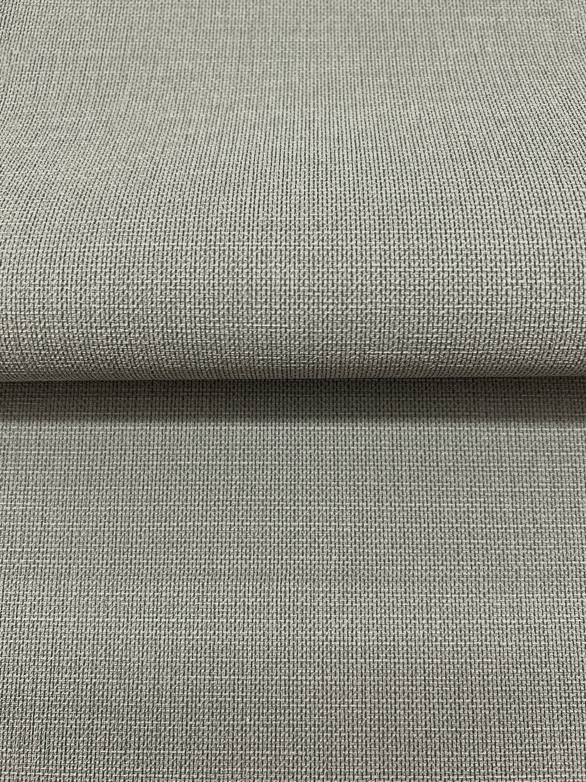 A folded piece of gray Magnolia Home Meadowbrook Wallpaper featuring a textured, woven fabric pattern.