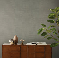 A wooden dresser holding a small vase, a decorative bowl, an open book, and a leafy green plant set against Magnolia Home Meadowbrook Wallpaper by York Wallcoverings.
