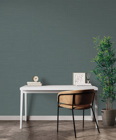 A white desk and a chair sit against a wall covered in dark green Magnolia Home Meadowbrook Wallpaper by York Wallcoverings.