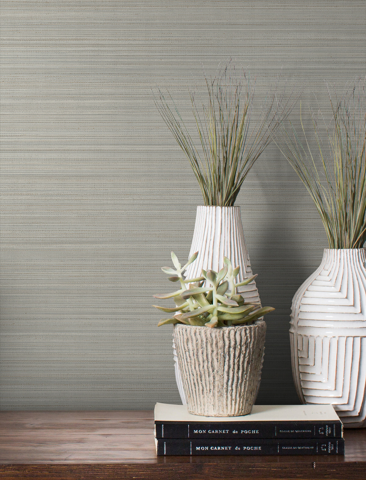 Magnolia Home Loomed Wallpaper with a gray, horizontal woven texture displayed behind two white vases, a succulent in a stone pot, and two stacked books on a wooden surface.