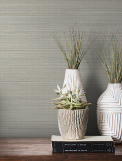 Magnolia Home Loomed Wallpaper with a gray, horizontal woven texture displayed behind two white vases, a succulent in a stone pot, and two stacked books on a wooden surface.