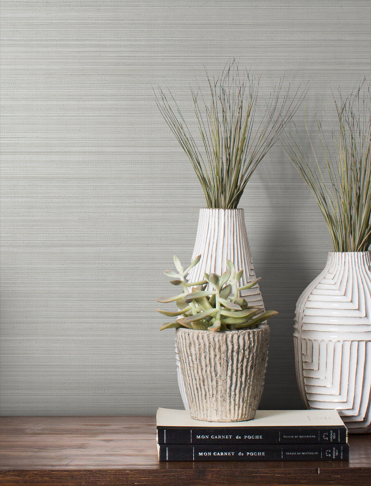 Magnolia Home Loomed Wallpaper in light gray with a fine, horizontal weave texture behind a shelf with two tall vases, a small succulent, and stacked books.
