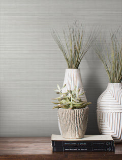 Magnolia Home Loomed Wallpaper in light gray with a fine, horizontal weave texture behind a shelf with two tall vases, a small succulent, and stacked books.