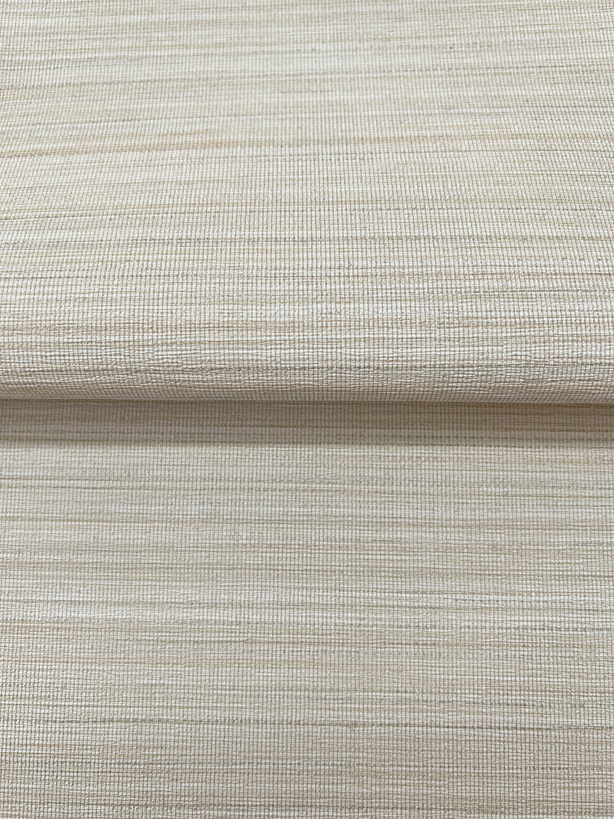 Close-up of a folded piece of beige Magnolia Home Loomed Wallpaper by York Wallcoverings, featuring a textured, woven-look horizontal pattern.