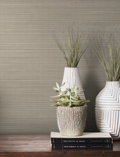 Magnolia Home Loomed Wallpaper in beige with a textured, horizontal weave pattern displayed behind two vases and a stack of books.