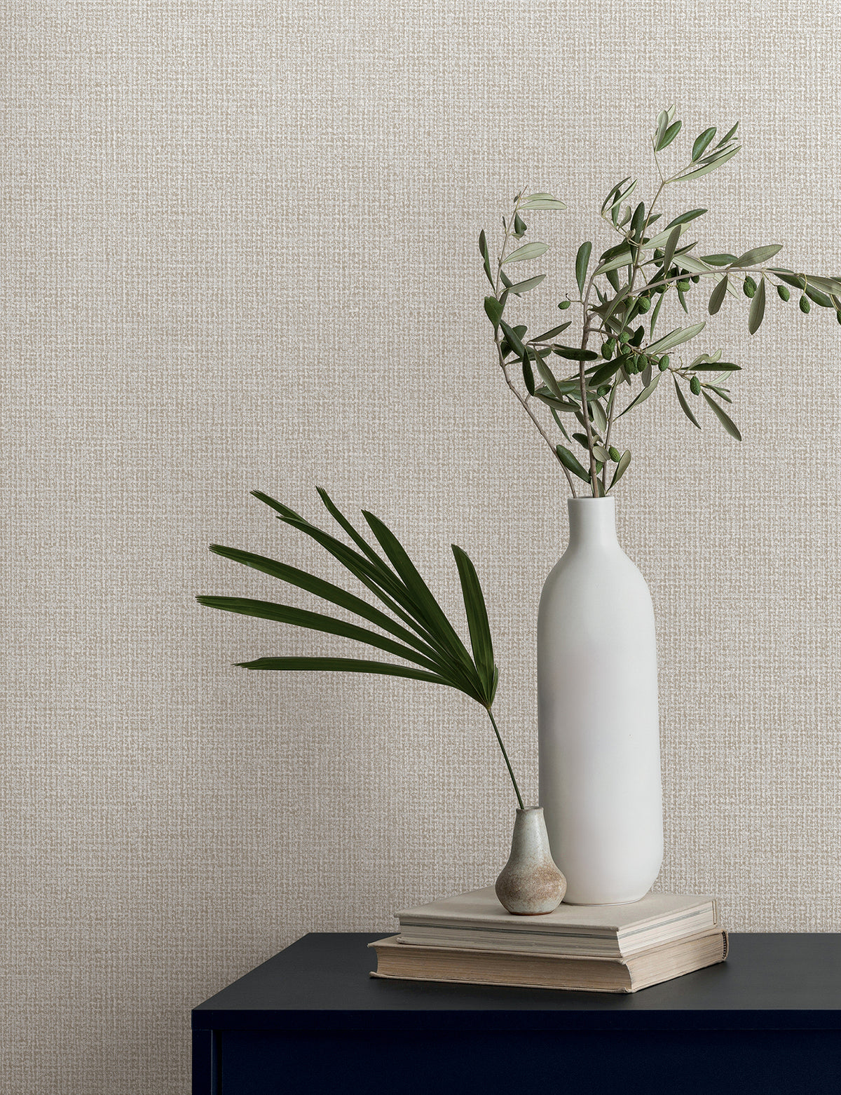 Two vases with green leaves sit on a stack of books against Magnolia Home Brindled Wallpaper by York Wallcoverings.