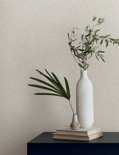 Two vases with green leaves sit on a stack of books against Magnolia Home Brindled Wallpaper by York Wallcoverings.